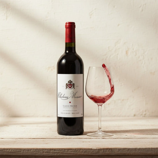 Bottle of Chateau Musar red wine with a poured glass on a wooden surface.