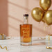 Bottle Cheers To The Best Dad Engraved Spiced Rum on a table with gold balloons and gift box in the background.