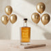 Bottle of Cheers To The Best Dad Engraved Whisky on a table with gold balloons in the background