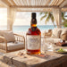 A bottle of Foursquare Penultimus Rum stands on a rustic wooden table in a beachside lounge setting. The amber liquid is visible through the clear bottle, with a black cap and a white label.