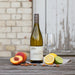 Bottle of Jaffelin Chardonnay with a glass, fruit, and nuts showcasing the flavours of the wine on a wooden table.