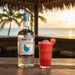 Mount Gay Silver rum bottle with a strawberry cocktail on a wooden table by the beach.