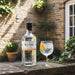 Sly Gin bottle with a glass of gin and tonic on a stone ledge outdoors.