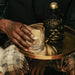 Person holding a glass of gin with a bottle of Still G.I.N. Gin By Dr. Dre & Snoop Dogg on a small round table.