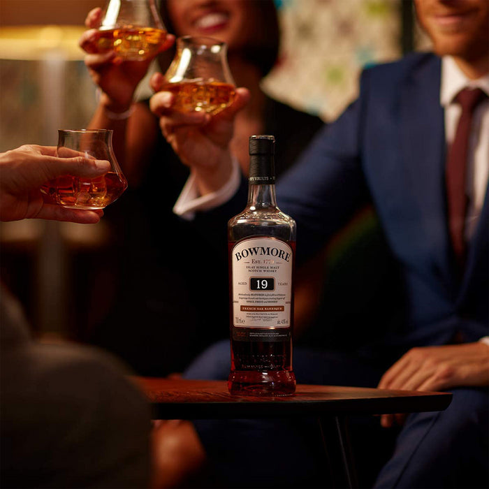 Bowmore 19 Year Old French Oak Barrique Whisky 70cl With Background Of Three people Enjoying Glasses Of Bowmore Whisky
