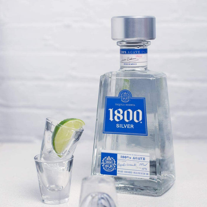 bottle of 1800 silver tequila reserva with shot glasses and lime wedge