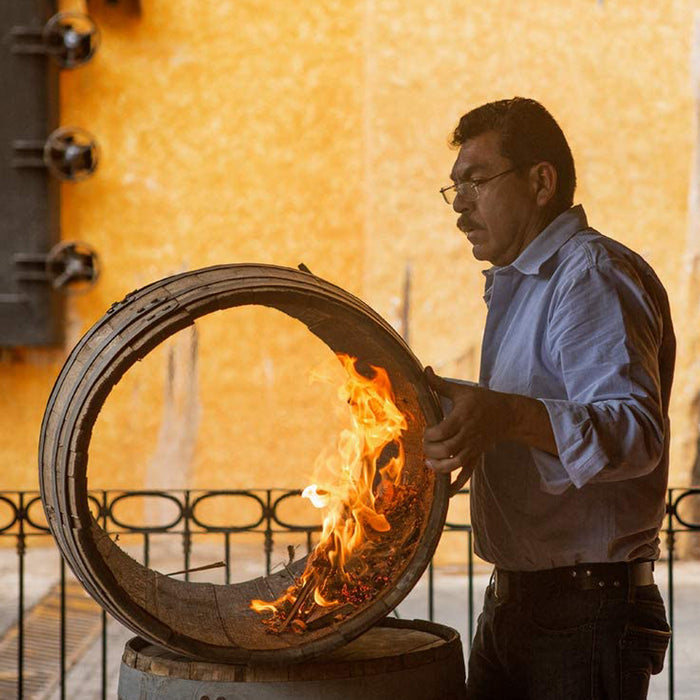 man spinning an open barrel with burning embers to char the inside of the barrel