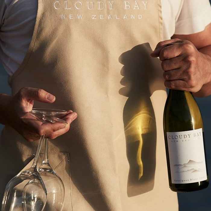 Someone holding a bottle of Cloudy Bay Sauvignon Blanc White Wine and two glasses